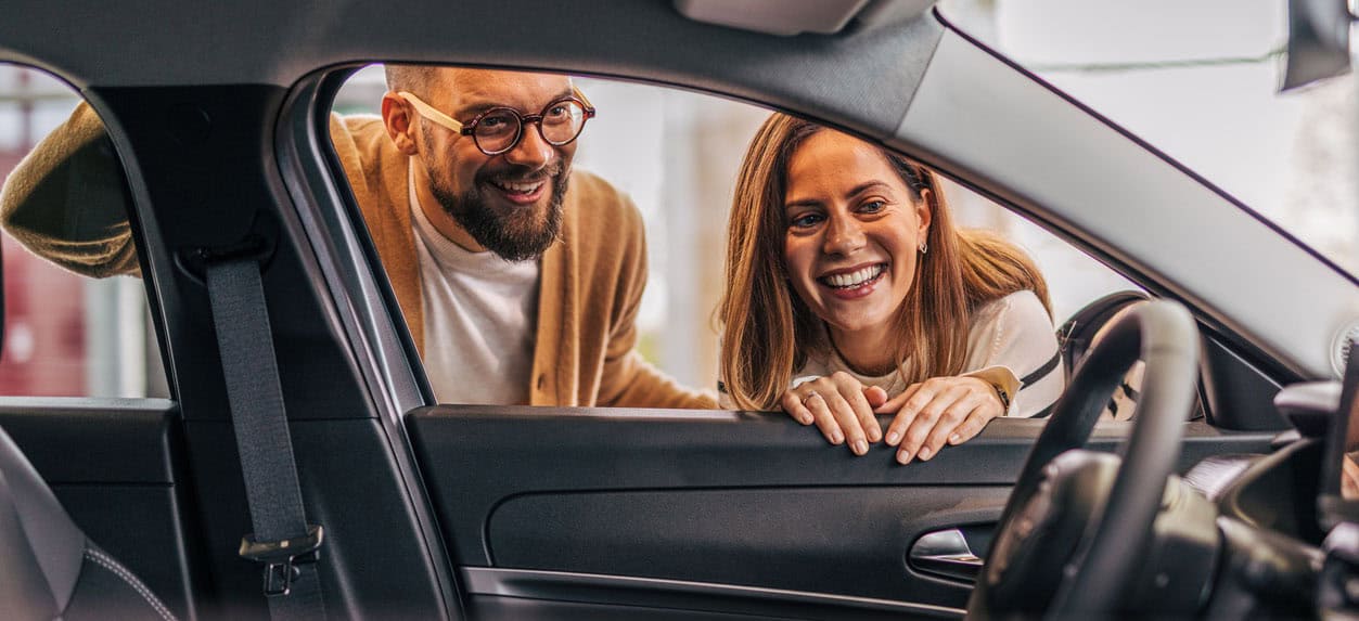A couple looking inside a new car at the dealership.