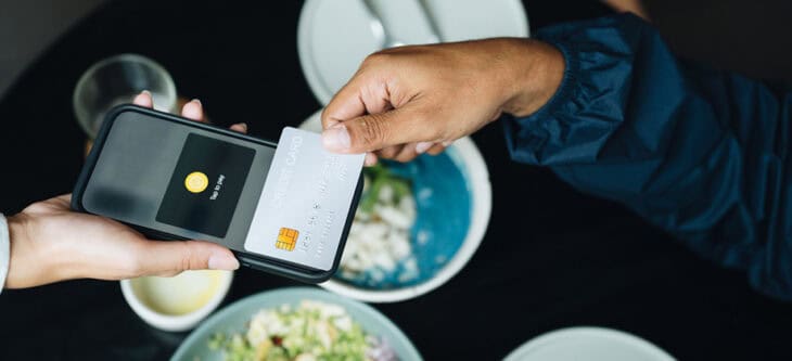 Close-up shot of man tapping a credit card on a smartphone to make a contactless payment at an organic healthy restaurant