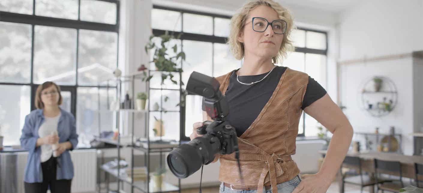 Professional Female Photographer With Camera In Modern Studio Space During Photo Session
