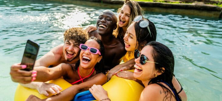 Friends taking selfies on the mobile phone on a swimming float in a swimming pool at a water park
